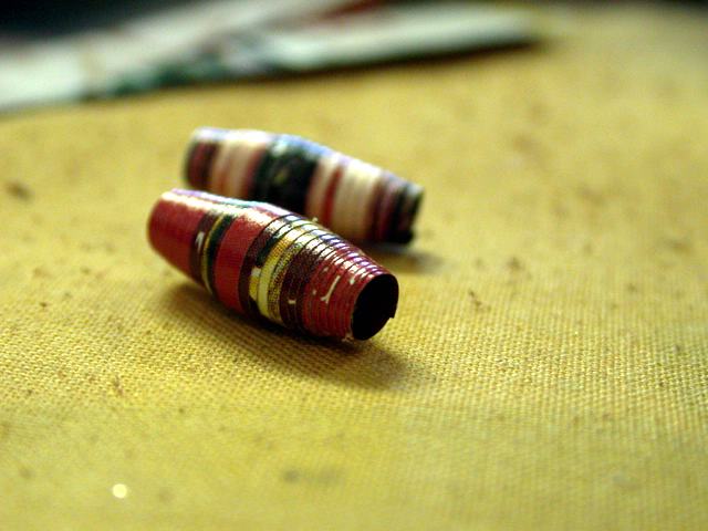 Perlen machen geht ganz einfach: Spitz zulaufenden Papierstreifen am breiten Ende beginnend auf einen Holzstab wickeln, Ende festkleben. Fertig.